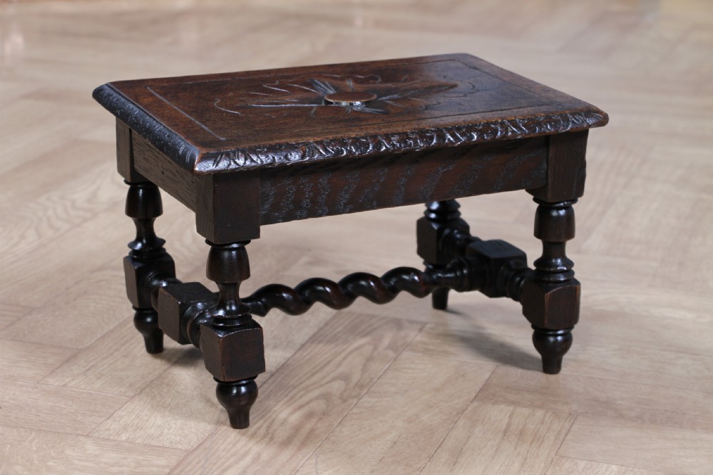 A small dark brown oak miniature stool with relief botanical carving on top, carved side aprons, turned legs, and a central barley twist stretcher. View III