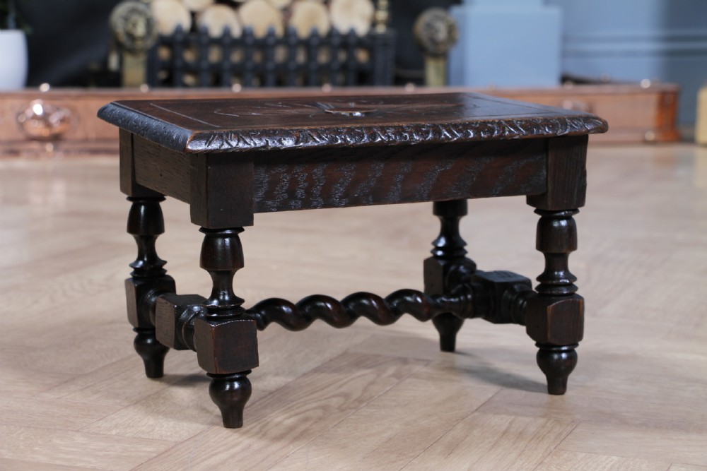 A small dark brown oak miniature stool with relief botanical carving on top, carved side aprons, turned legs, and a central barley twist stretcher. View IV