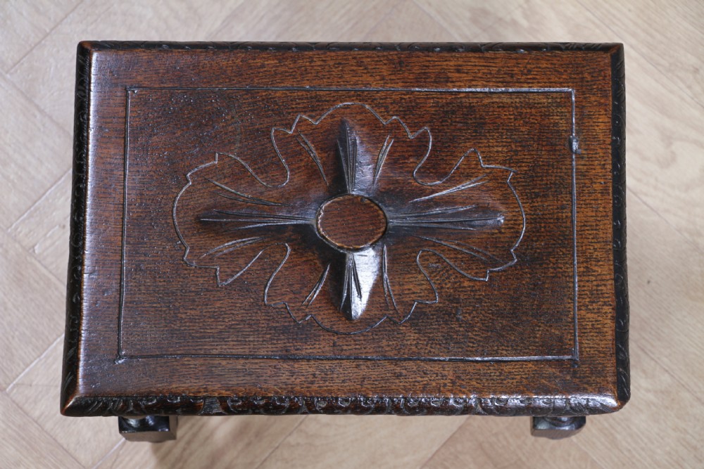 A small dark brown oak miniature stool with relief botanical carving on top, carved side aprons, turned legs, and a central barley twist stretcher. View V