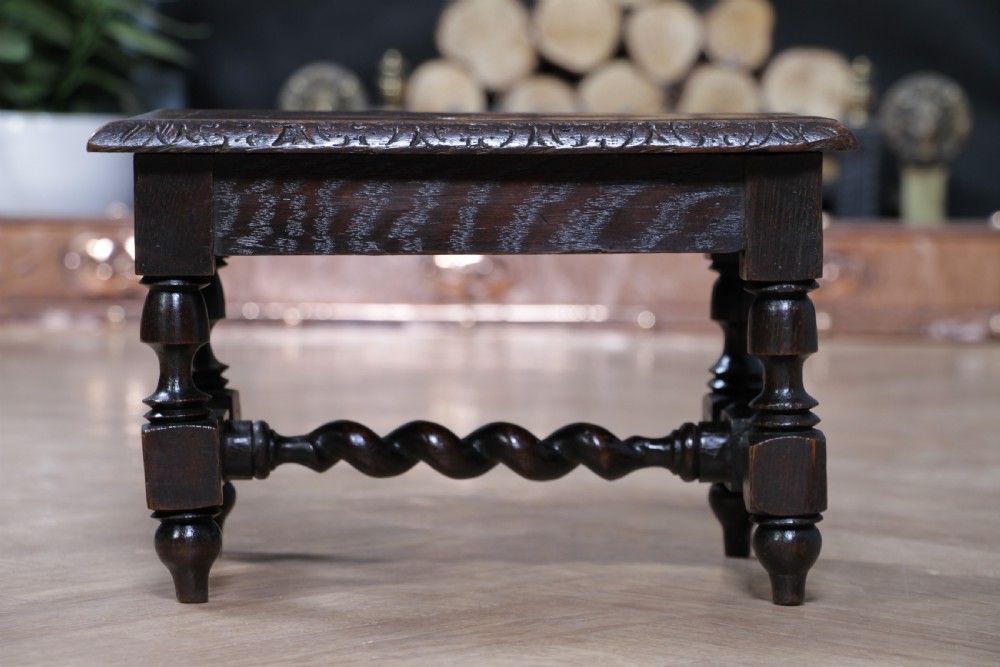 A small dark brown oak miniature stool with relief botanical carving on top, carved side aprons, turned legs, and a central barley twist stretcher. View VIII