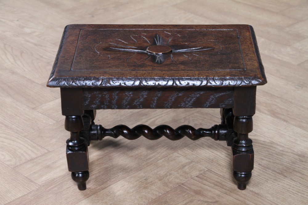 A small dark brown oak miniature stool with relief botanical carving on top, carved side aprons, turned legs, and a central barley twist stretcher. View IX