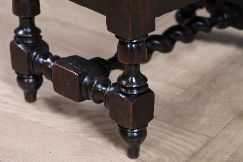 A small dark brown oak miniature stool with relief botanical carving on top, carved side aprons, turned legs, and a central barley twist stretcher. View XI