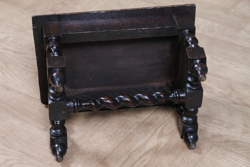 A small dark brown oak miniature stool with relief botanical carving on top, carved side aprons, turned legs, and a central barley twist stretcher. View XII