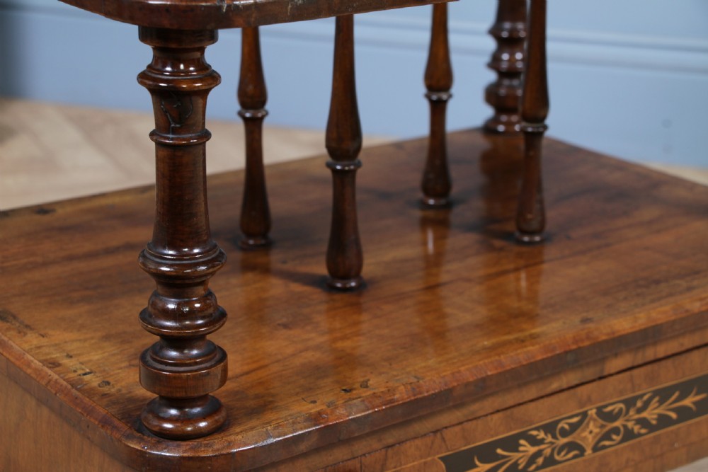 A Victorian burr walnut Canterbury whatnot featuring a flat top surface, turned supports, vertical dividers, a bottom drawer with inlaid motifs, and brass castors. View XIII