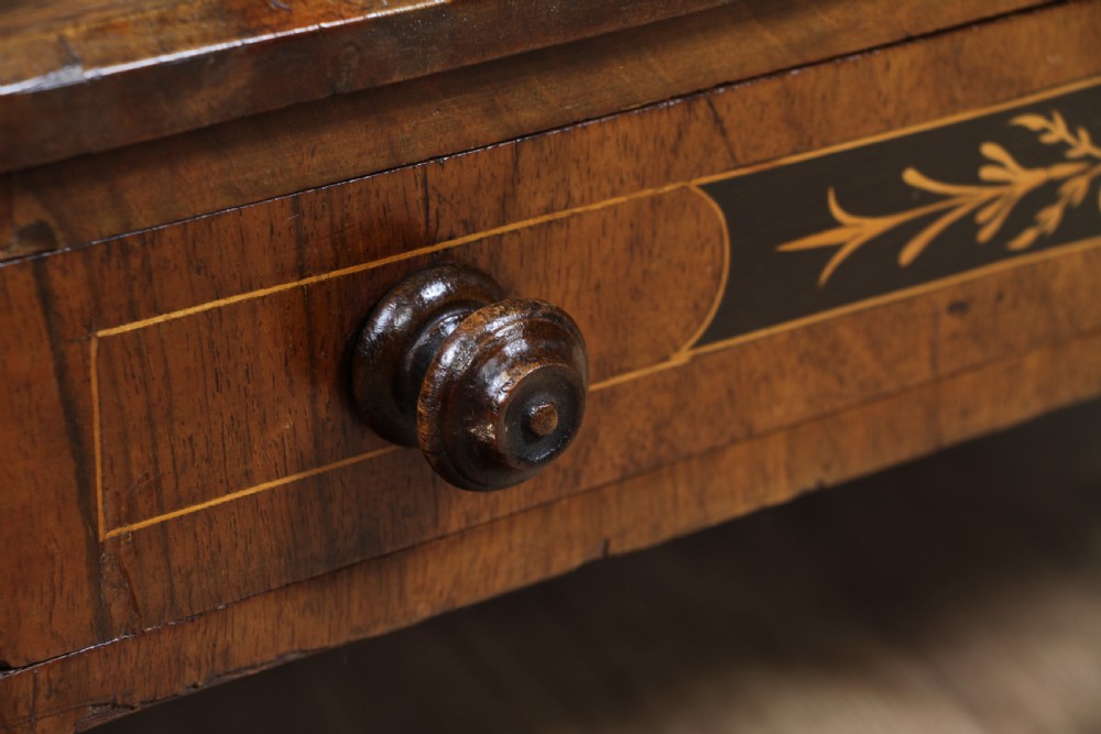 A Victorian burr walnut Canterbury whatnot featuring a flat top surface, turned supports, vertical dividers, a bottom drawer with inlaid motifs, and brass castors. View XIV