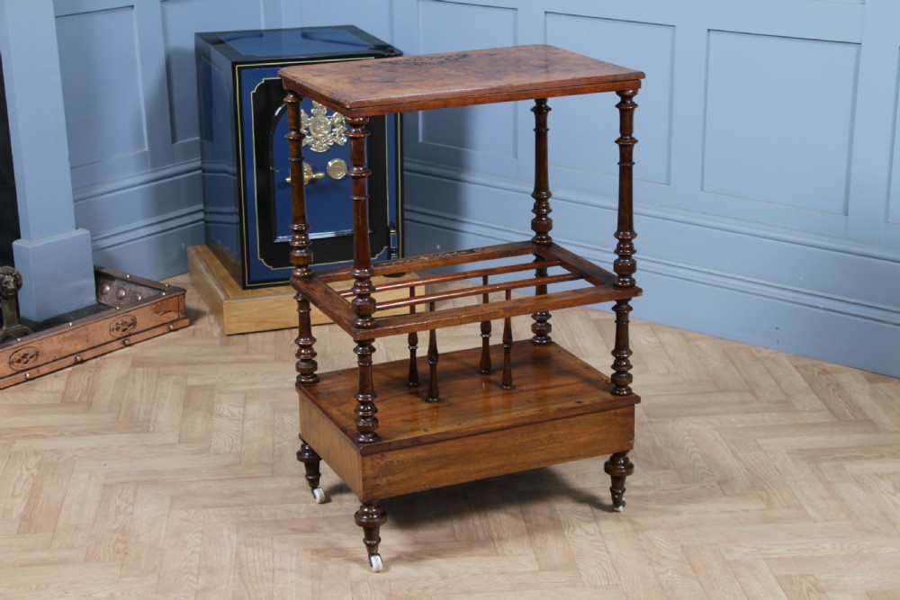 A Victorian burr walnut Canterbury whatnot featuring a flat top surface, turned supports, vertical dividers, a bottom drawer with inlaid motifs, and brass castors. View XXIII