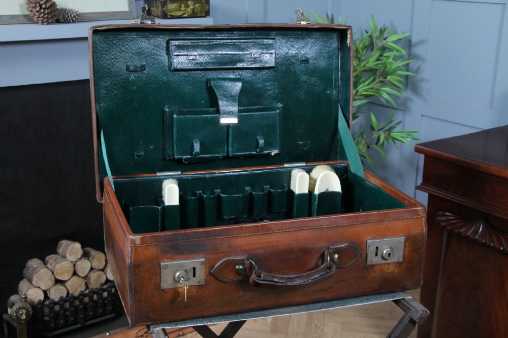 A rectangular chestnut brown leather suitcase with brass slide latches, a central leather handle, and black stencilled lettering reading C. ANTROBUS. View II