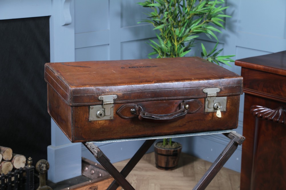 A rectangular chestnut brown leather suitcase with brass slide latches, a central leather handle, and black stencilled lettering reading C. ANTROBUS. View III