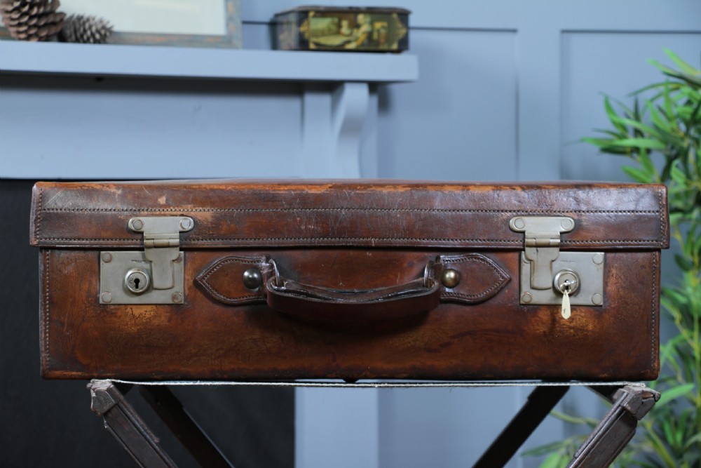 A rectangular chestnut brown leather suitcase with brass slide latches, a central leather handle, and black stencilled lettering reading C. ANTROBUS. View VI