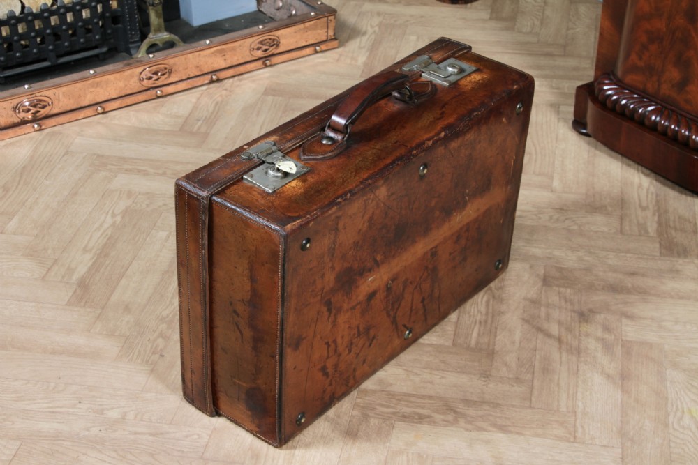 A rectangular chestnut brown leather suitcase with brass slide latches, a central leather handle, and black stencilled lettering reading C. ANTROBUS. View VIII