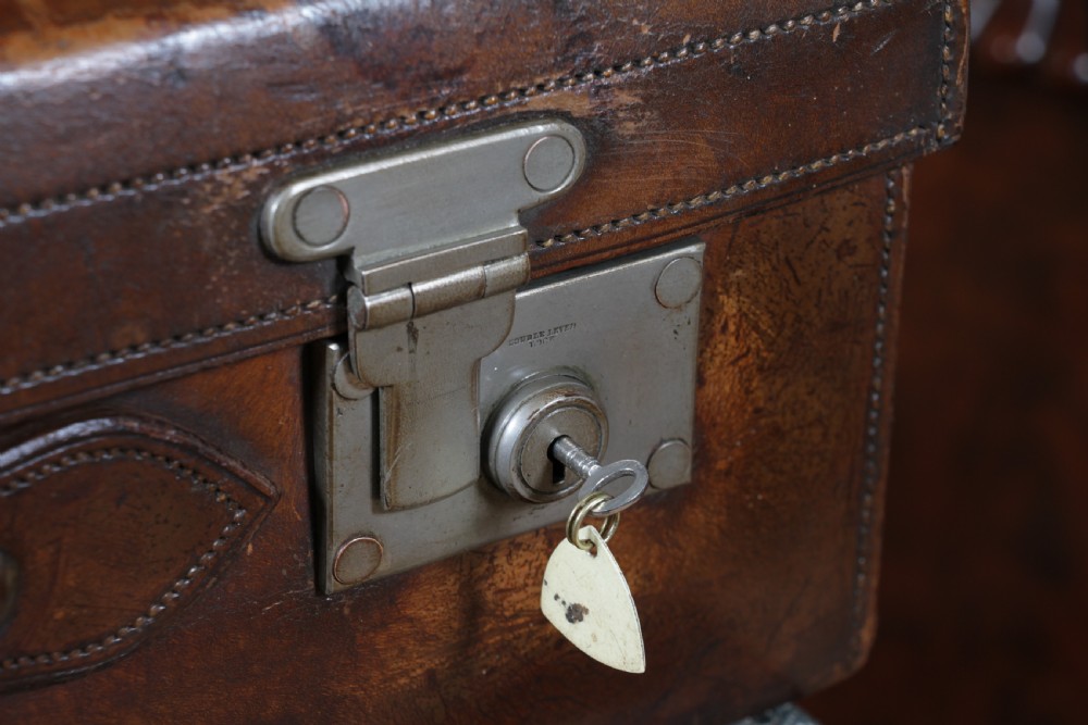 A rectangular chestnut brown leather suitcase with brass slide latches, a central leather handle, and black stencilled lettering reading C. ANTROBUS. View IX