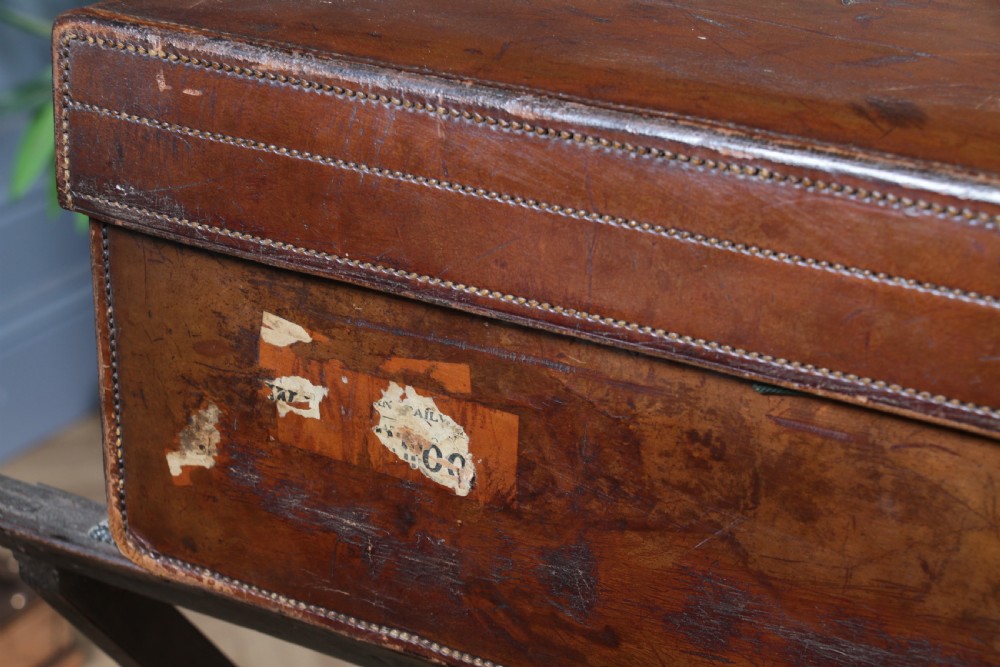 A rectangular chestnut brown leather suitcase with brass slide latches, a central leather handle, and black stencilled lettering reading C. ANTROBUS. View XII