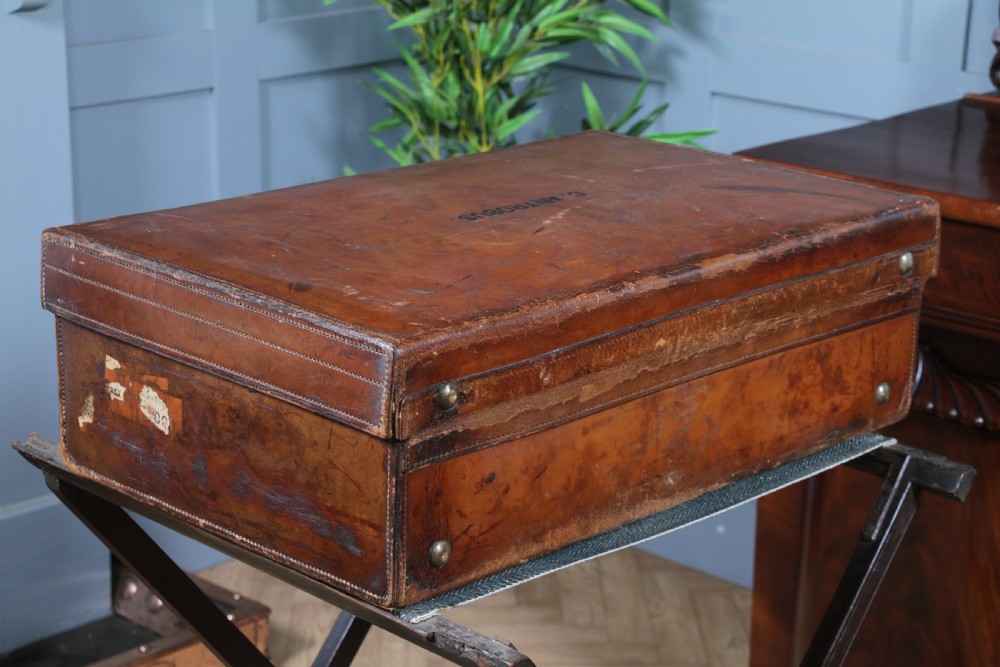 A rectangular chestnut brown leather suitcase with brass slide latches, a central leather handle, and black stencilled lettering reading C. ANTROBUS. View XIII