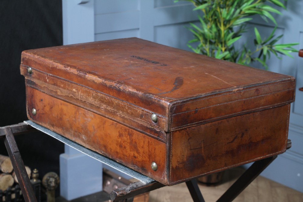 A rectangular chestnut brown leather suitcase with brass slide latches, a central leather handle, and black stencilled lettering reading C. ANTROBUS. View XIV