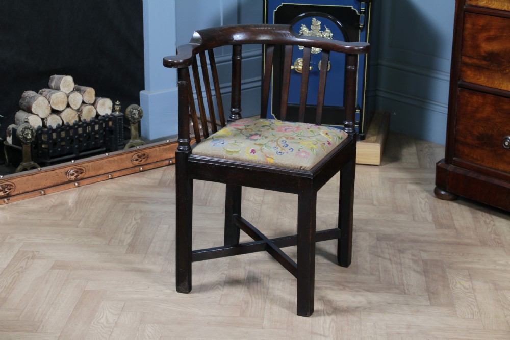 A dark elm Georgian corner chair with a curved top rail, slat back structure, turned supports, cross stretchers, and a floral tapestry drop-in seat.
