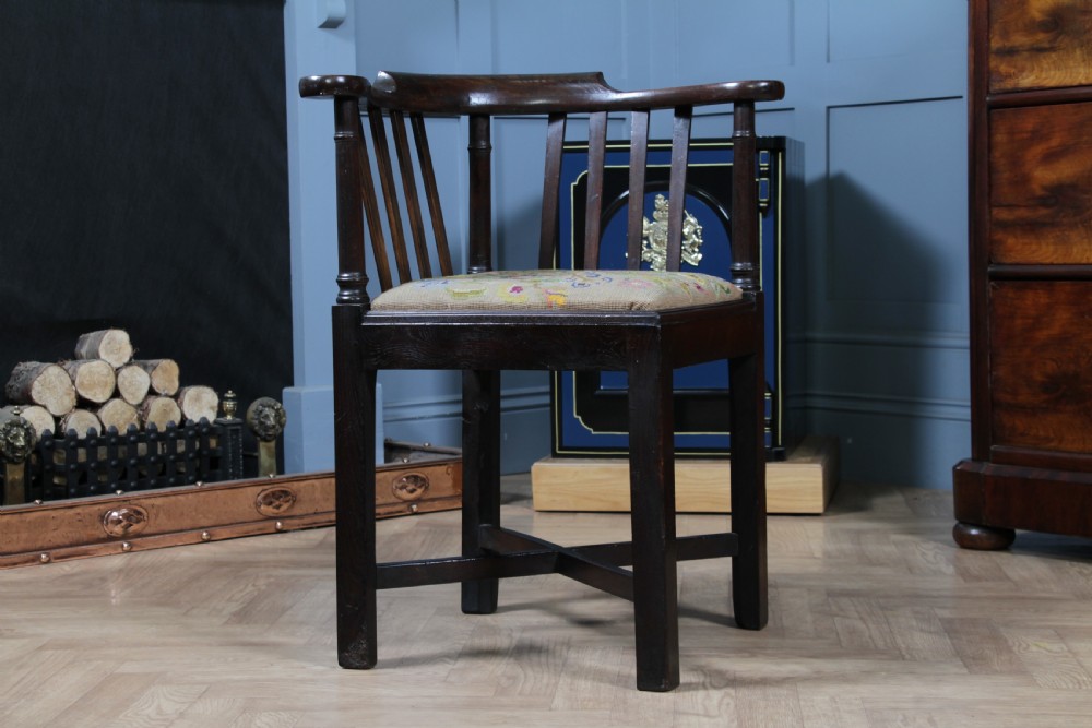 A dark elm Georgian corner chair with a curved top rail, slat back structure, turned supports, cross stretchers, and a floral tapestry drop-in seat. View III