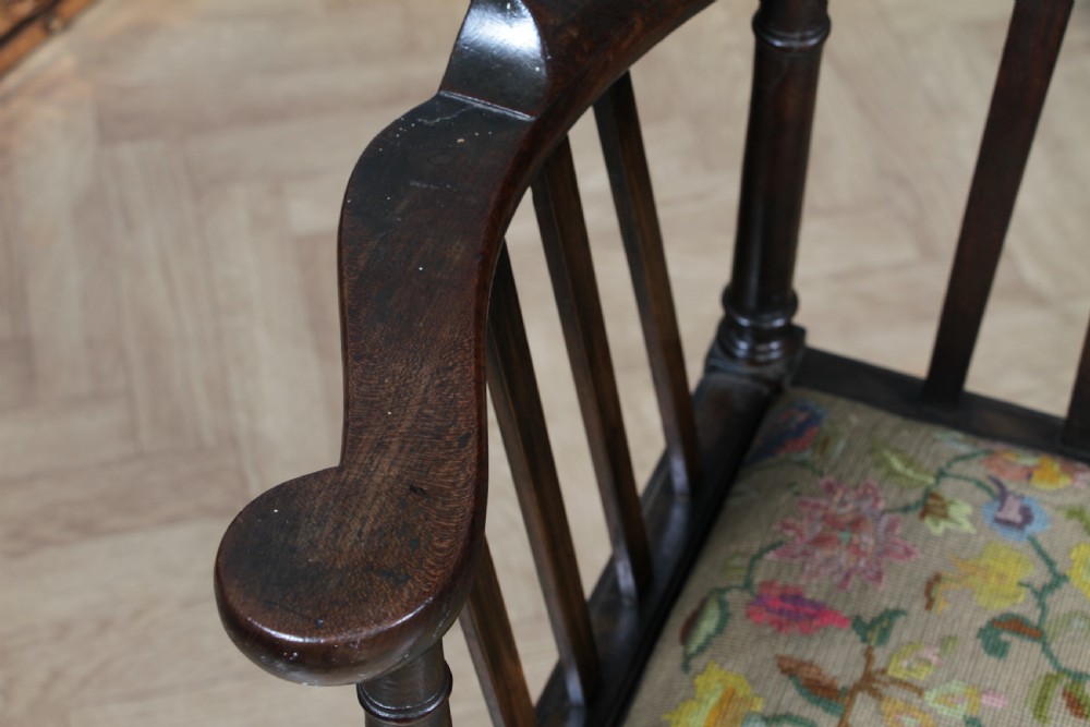 A dark elm Georgian corner chair with a curved top rail, slat back structure, turned supports, cross stretchers, and a floral tapestry drop-in seat. View V