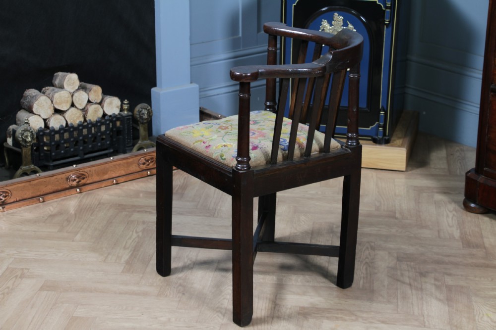 A dark elm Georgian corner chair with a curved top rail, slat back structure, turned supports, cross stretchers, and a floral tapestry drop-in seat. View VI