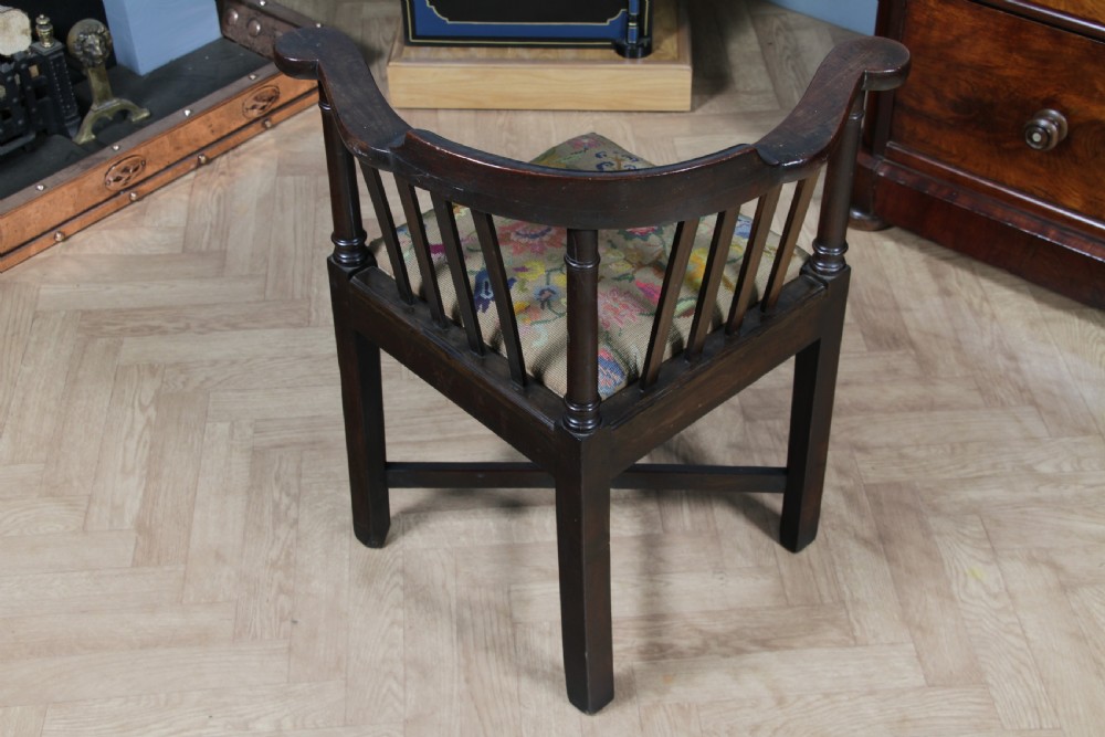 A dark elm Georgian corner chair with a curved top rail, slat back structure, turned supports, cross stretchers, and a floral tapestry drop-in seat. View VII
