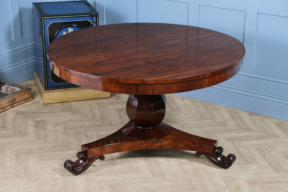 A circular dark rosewood centre table featuring a polished surface, a central bulbous faceted pedestal, and a triform base resting on carved scroll feet.