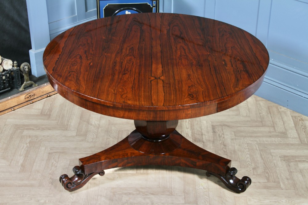 A circular dark rosewood centre table featuring a polished surface, a central bulbous faceted pedestal, and a triform base resting on carved scroll feet. View II