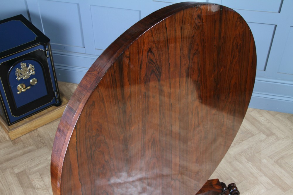 A circular dark rosewood centre table featuring a polished surface, a central bulbous faceted pedestal, and a triform base resting on carved scroll feet. View VI