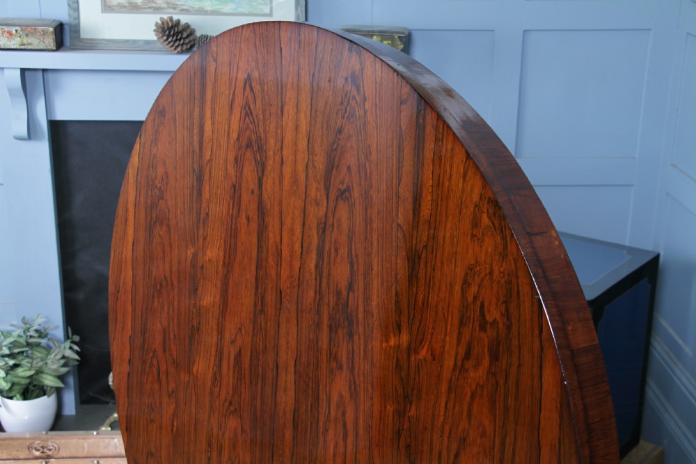 A circular dark rosewood centre table featuring a polished surface, a central bulbous faceted pedestal, and a triform base resting on carved scroll feet. View VII