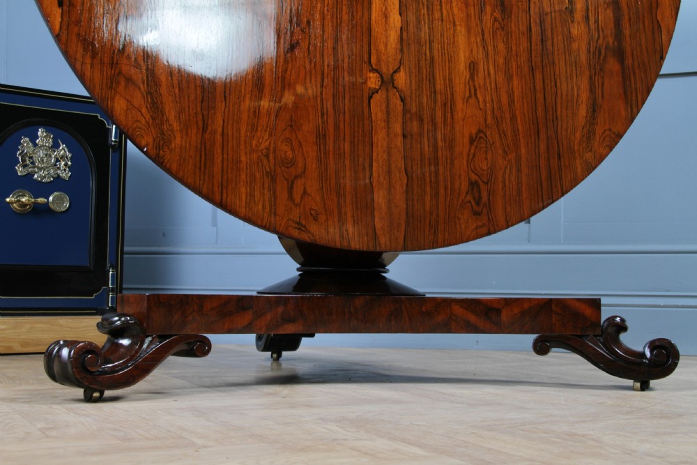 A circular dark rosewood centre table featuring a polished surface, a central bulbous faceted pedestal, and a triform base resting on carved scroll feet. View VIII