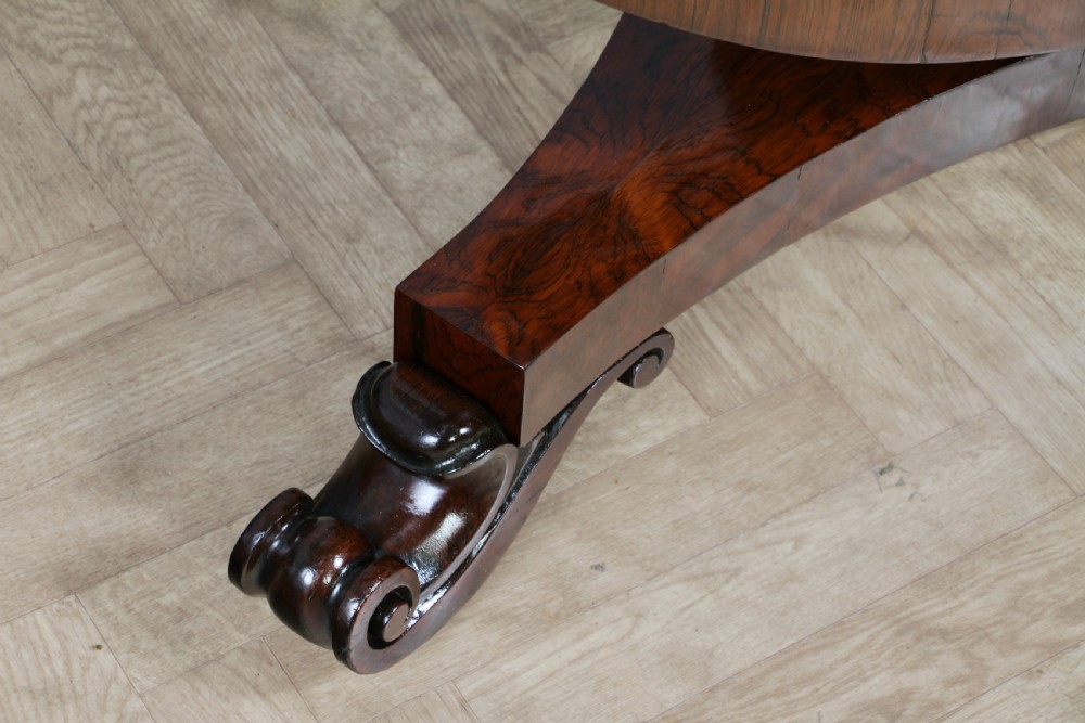 A circular dark rosewood centre table featuring a polished surface, a central bulbous faceted pedestal, and a triform base resting on carved scroll feet. View XIII