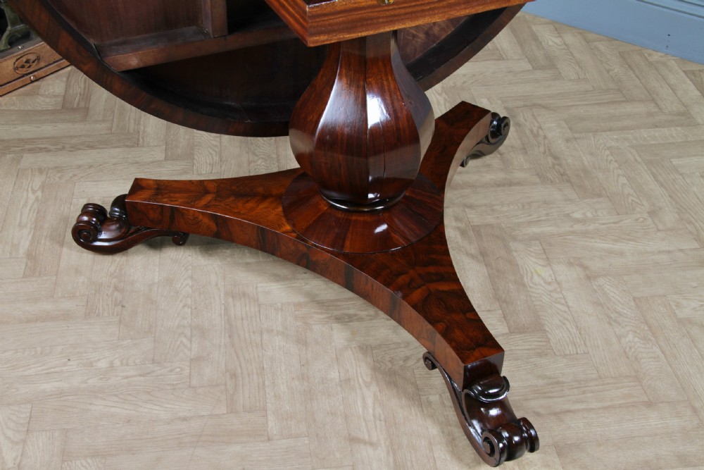 A circular dark rosewood centre table featuring a polished surface, a central bulbous faceted pedestal, and a triform base resting on carved scroll feet. View XV