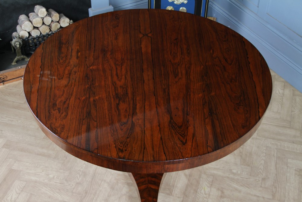 A circular dark rosewood centre table featuring a polished surface, a central bulbous faceted pedestal, and a triform base resting on carved scroll feet. View XVII