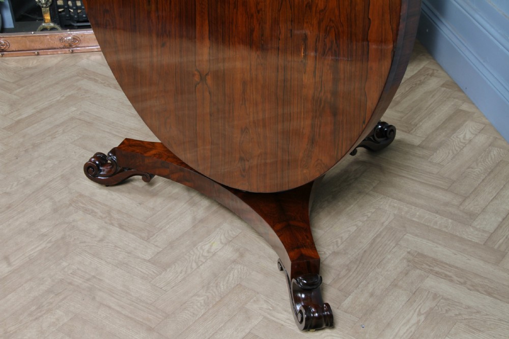 A circular dark rosewood centre table featuring a polished surface, a central bulbous faceted pedestal, and a triform base resting on carved scroll feet. View XVIII