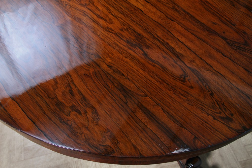 A circular dark rosewood centre table featuring a polished surface, a central bulbous faceted pedestal, and a triform base resting on carved scroll feet. View XIX