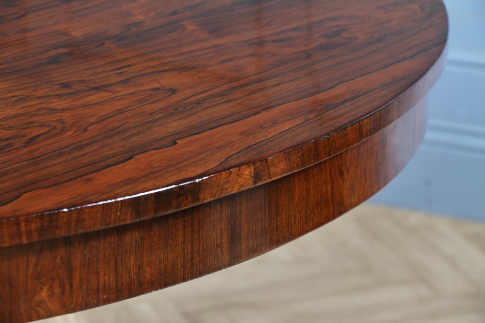 A circular dark rosewood centre table featuring a polished surface, a central bulbous faceted pedestal, and a triform base resting on carved scroll feet. View XX