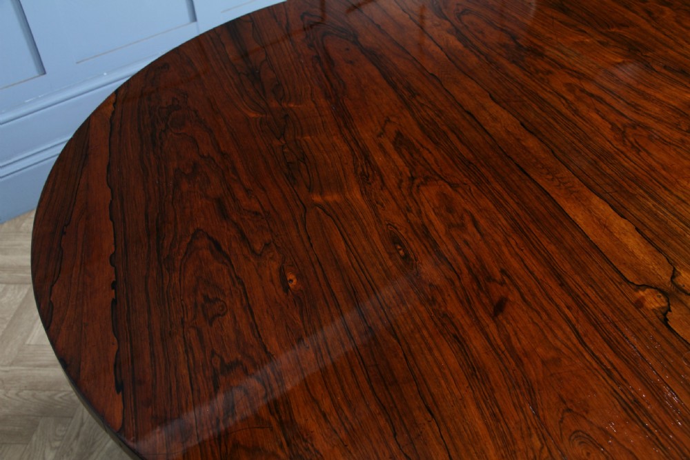 A circular dark rosewood centre table featuring a polished surface, a central bulbous faceted pedestal, and a triform base resting on carved scroll feet. View XXII
