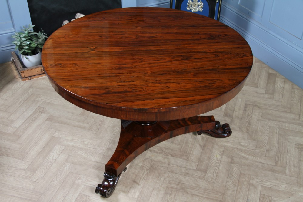 A circular dark rosewood centre table featuring a polished surface, a central bulbous faceted pedestal, and a triform base resting on carved scroll feet. View XXIV
