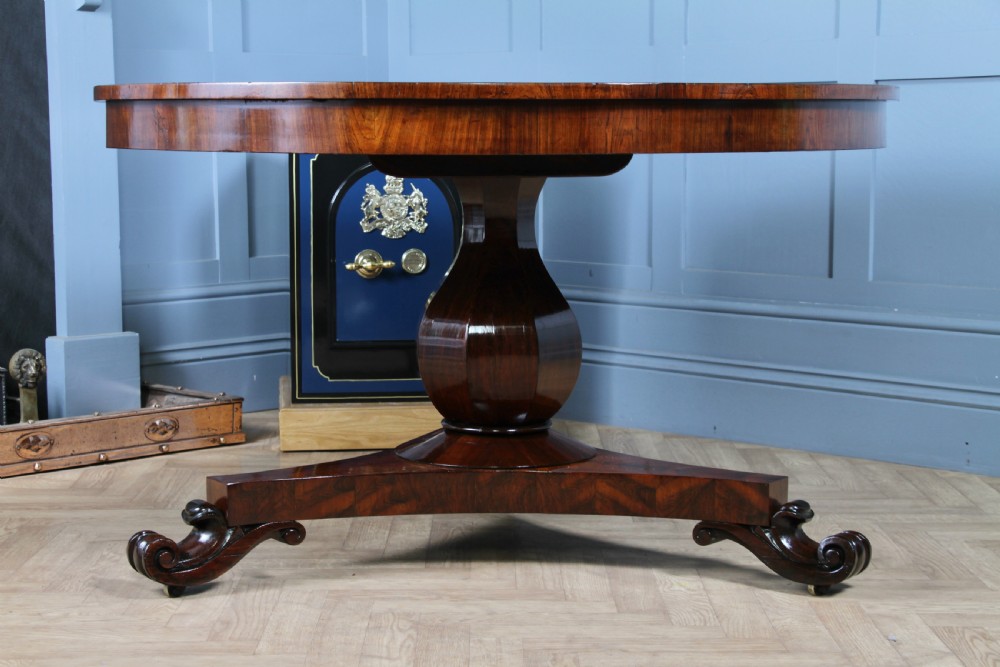 A circular dark rosewood centre table featuring a polished surface, a central bulbous faceted pedestal, and a triform base resting on carved scroll feet. View XXV