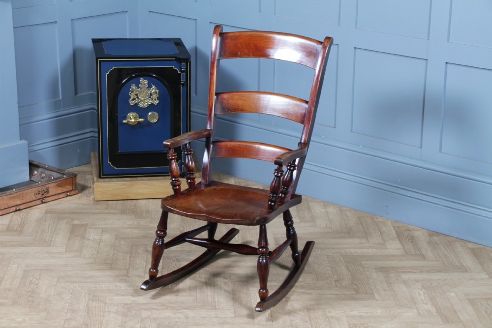 An antique Victorian ladder-back wooden rocking chair with three horizontal back slats, turned spindle arm supports, and curved rockers.
