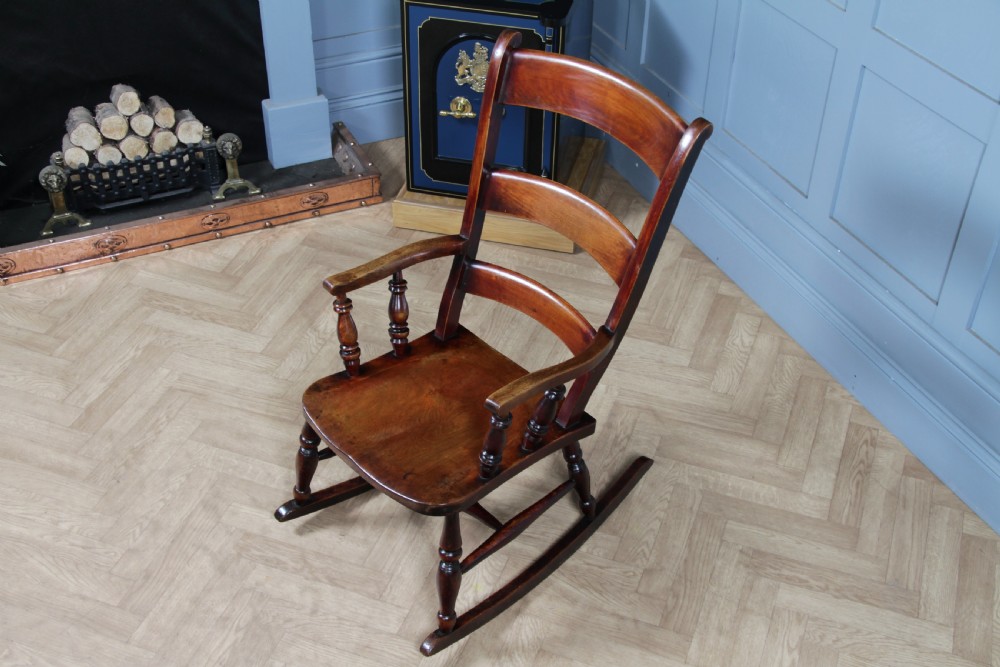 An antique Victorian ladder-back wooden rocking chair with three horizontal back slats, turned spindle arm supports, and curved rockers. View II