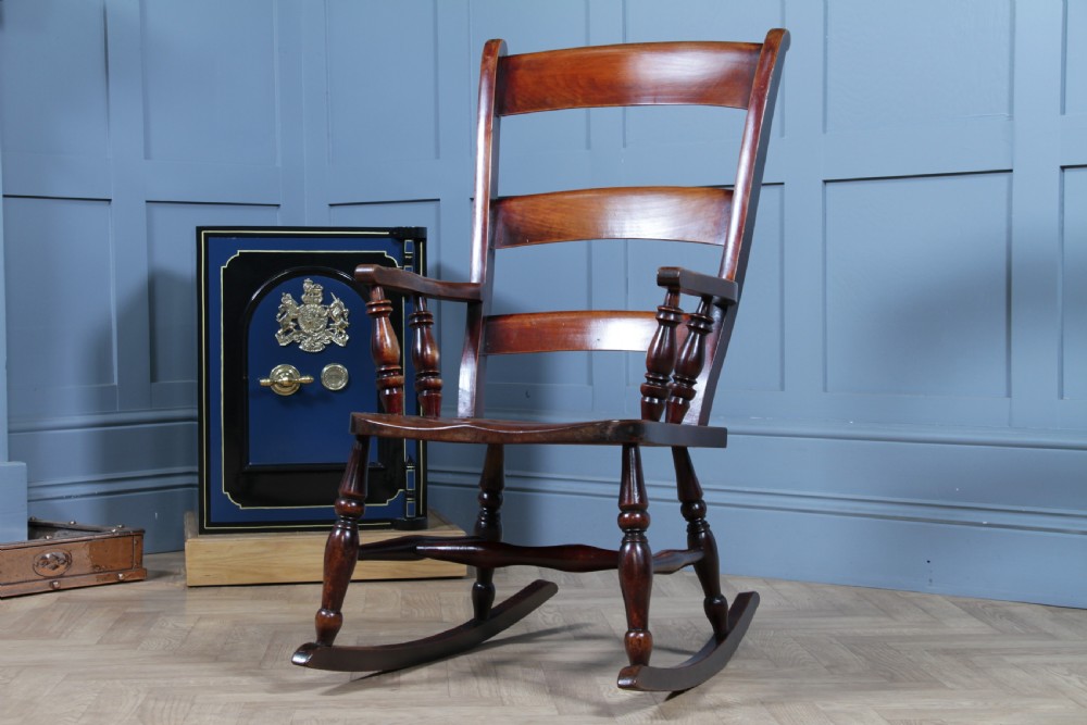 An antique Victorian ladder-back wooden rocking chair with three horizontal back slats, turned spindle arm supports, and curved rockers. View III