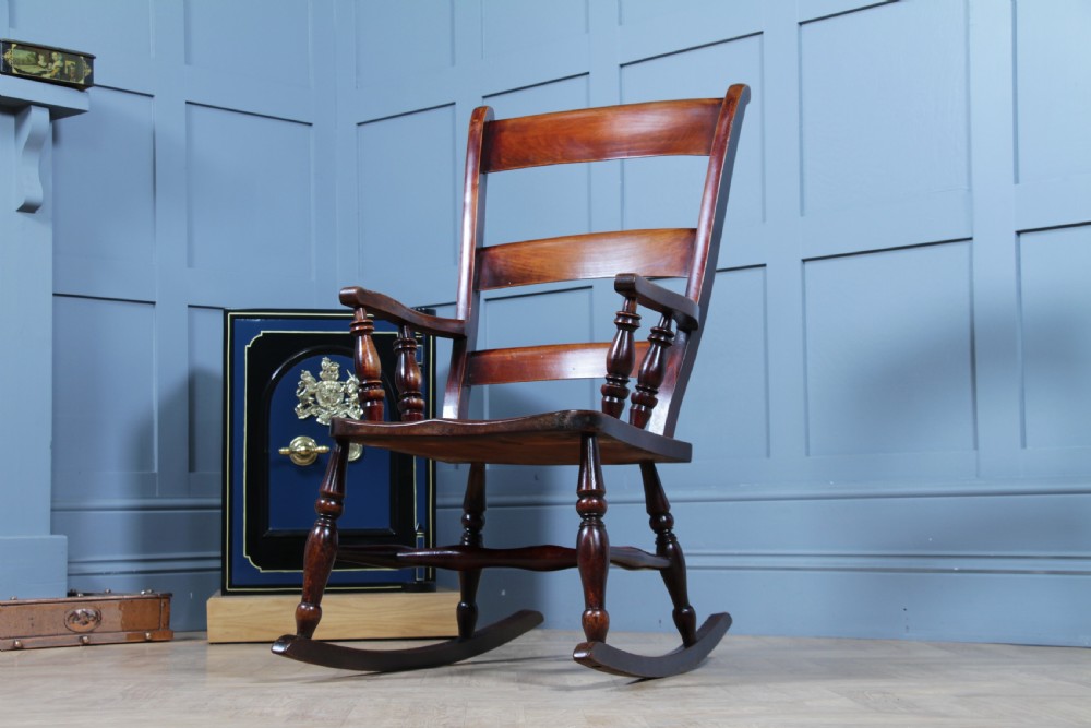 An antique Victorian ladder-back wooden rocking chair with three horizontal back slats, turned spindle arm supports, and curved rockers. View IV