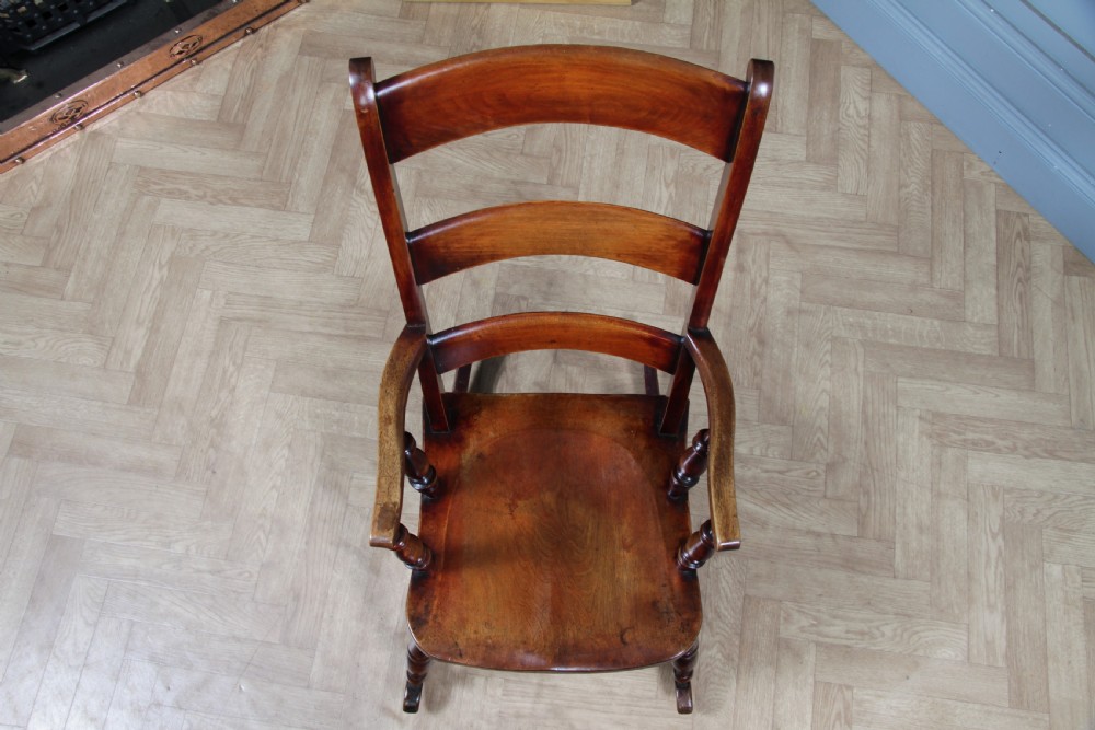 An antique Victorian ladder-back wooden rocking chair with three horizontal back slats, turned spindle arm supports, and curved rockers. View V