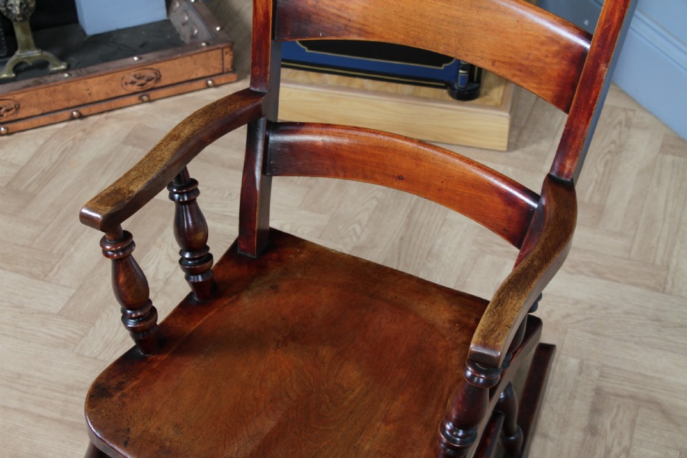 An antique Victorian ladder-back wooden rocking chair with three horizontal back slats, turned spindle arm supports, and curved rockers. View IX