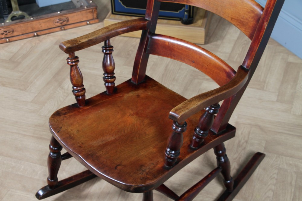 An antique Victorian ladder-back wooden rocking chair with three horizontal back slats, turned spindle arm supports, and curved rockers. View X