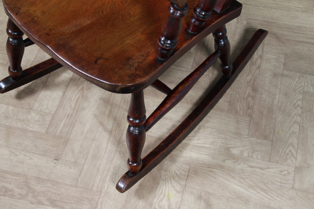 An antique Victorian ladder-back wooden rocking chair with three horizontal back slats, turned spindle arm supports, and curved rockers. View XI