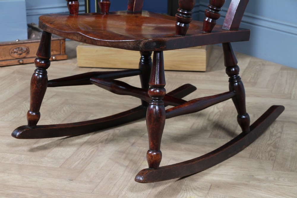An antique Victorian ladder-back wooden rocking chair with three horizontal back slats, turned spindle arm supports, and curved rockers. View XII
