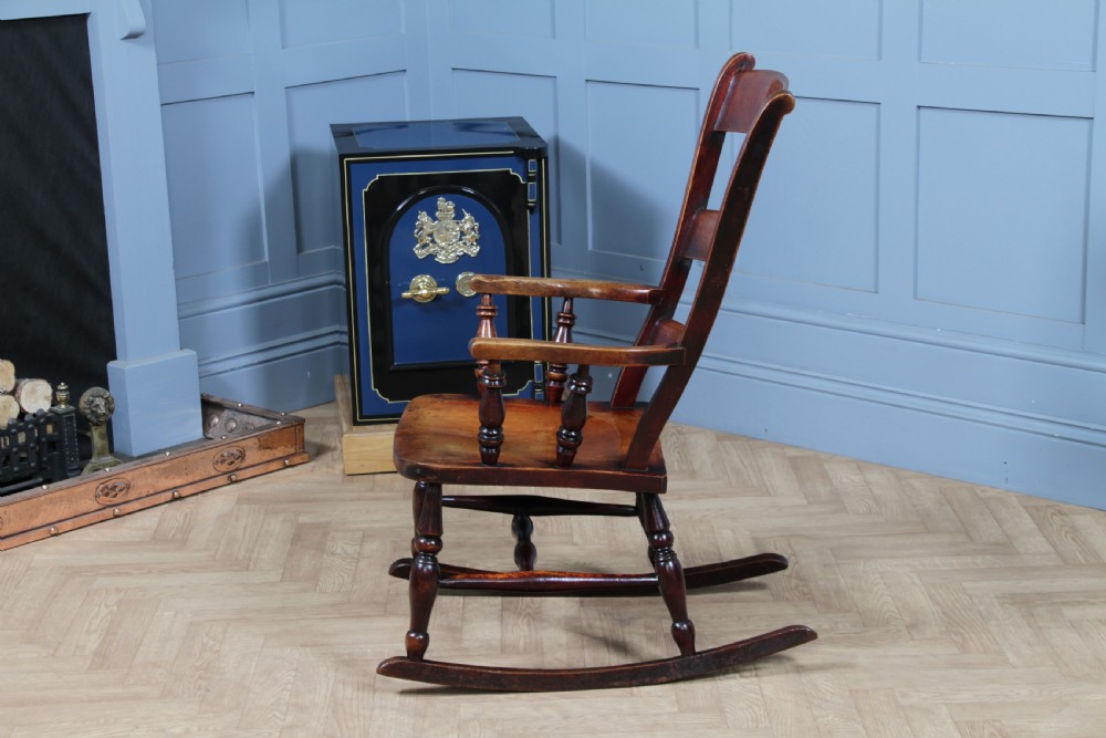 An antique Victorian ladder-back wooden rocking chair with three horizontal back slats, turned spindle arm supports, and curved rockers. View XIV
