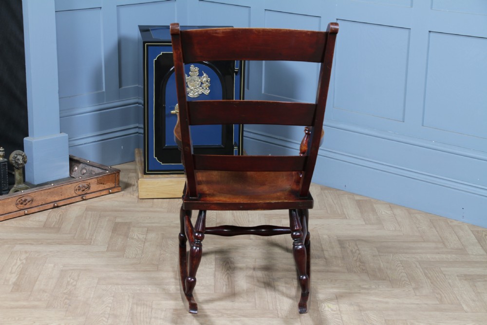 An antique Victorian ladder-back wooden rocking chair with three horizontal back slats, turned spindle arm supports, and curved rockers. View XVI
