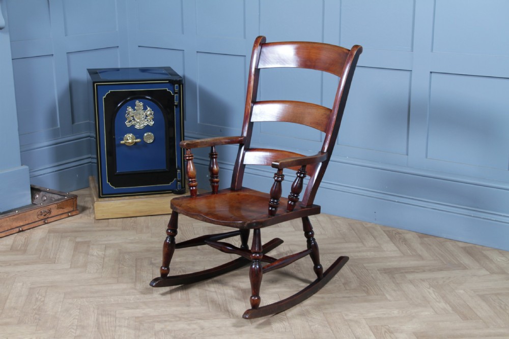 An antique Victorian ladder-back wooden rocking chair with three horizontal back slats, turned spindle arm supports, and curved rockers. View XVII