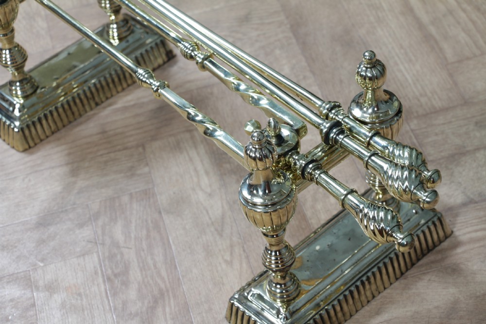 A late Victorian polished brass companion set featuring a shovel, tongs, and poker supported horizontally across two urn-topped brass firedogs. View IV